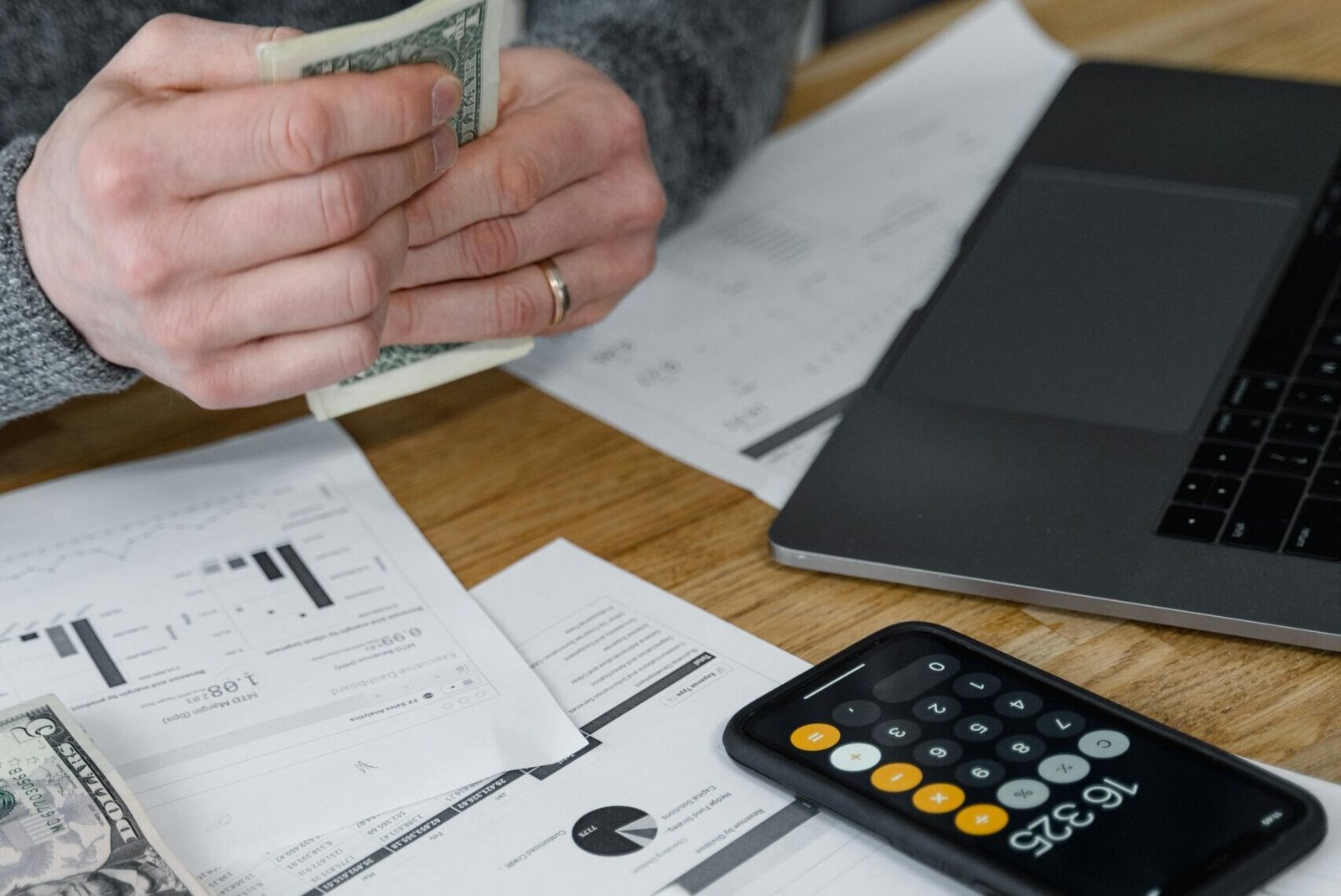 Hands counting money at a workspace with a laptop, calculator, and financial documents.